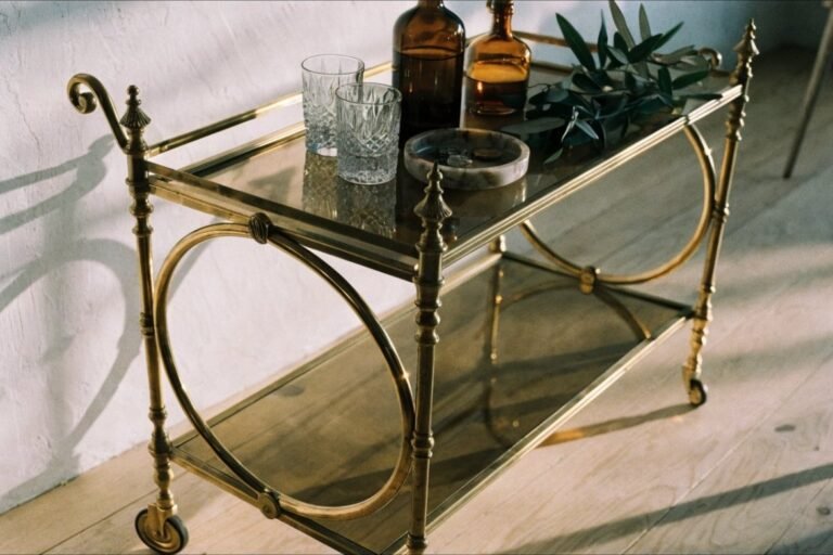 An antique brass and smoked-glass bar cart styled with crystal glasses and amber bottles