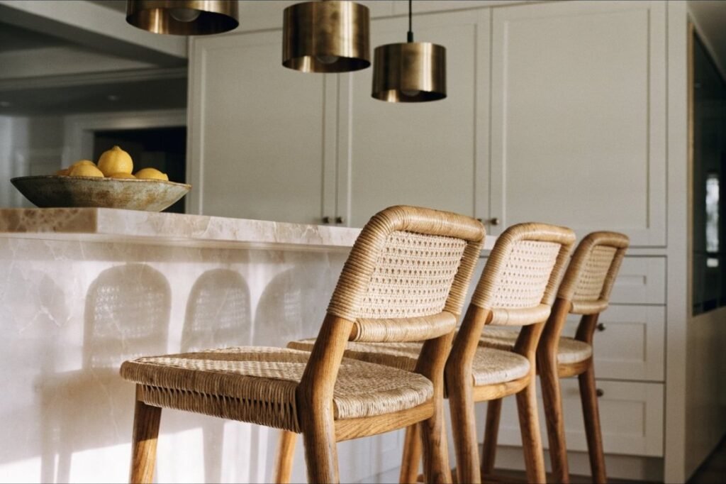 Three woven rush counter stools with oak legs tucked under a honed marble kitchen island