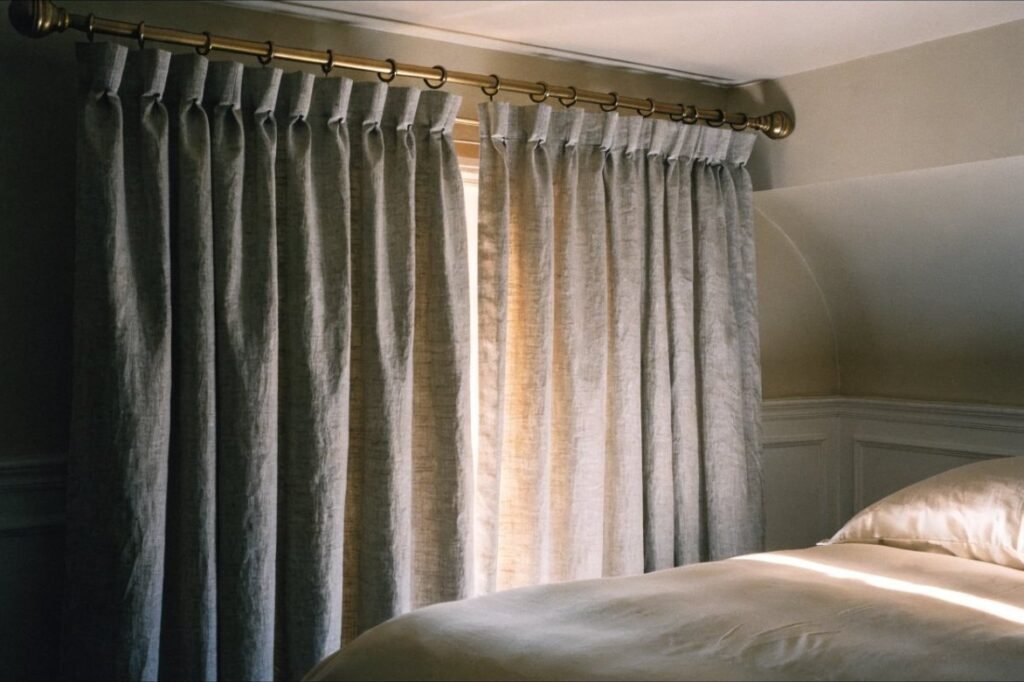 Heavyweight greige linen-look blackout curtains drawn nearly closed in a serene bedroom