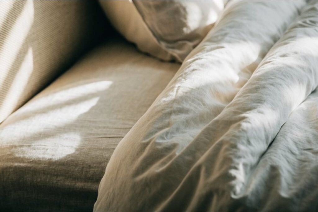 A warm white washed-cotton duvet cover folded back over oatmeal linen sheets in morning light