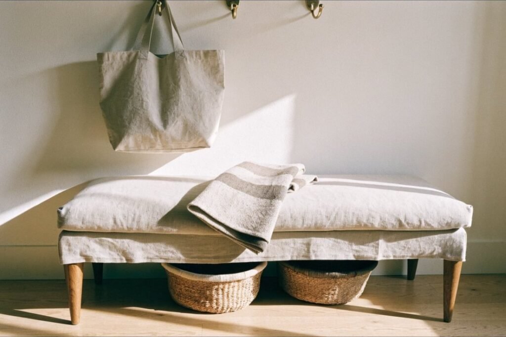 An oatmeal linen bench with oak legs, woven baskets beneath and brass hooks above