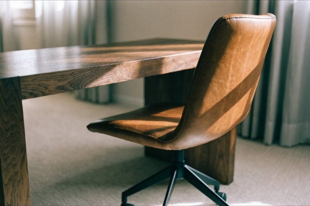 A low-back caramel leather desk chair with a matte black swivel base at a walnut desk