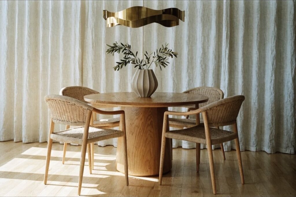 A round oak pedestal dining table with woven-back chairs and a brass pendant above