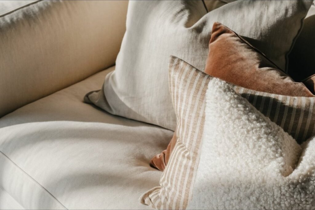Throw pillows in oatmeal linen, ivory boucle, a tonal stripe and clay velvet layered on a cream sofa