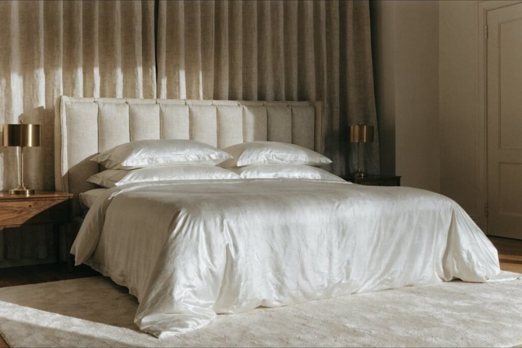 A generously scaled bed with a channel-tufted oatmeal linen headboard, flanked by walnut nightstands
