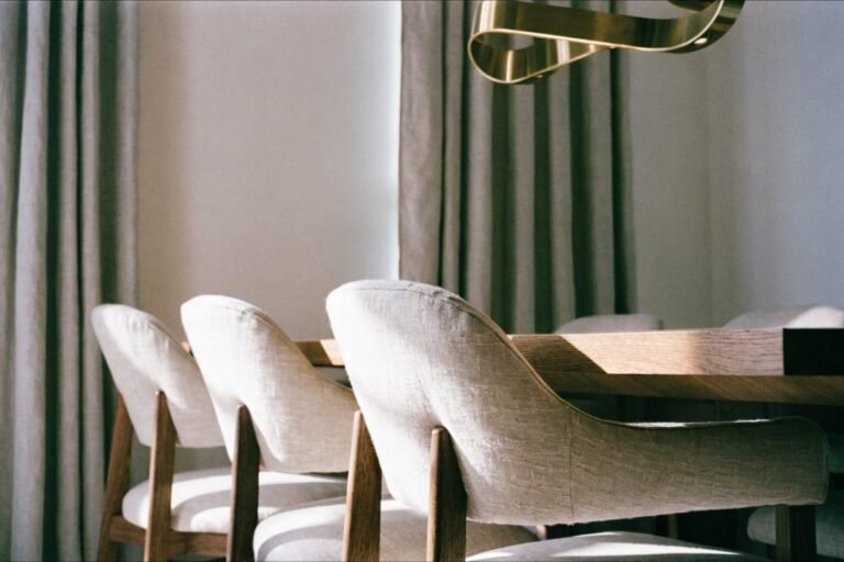 Four oatmeal linen upholstered dining chairs with walnut legs at a warm oak table