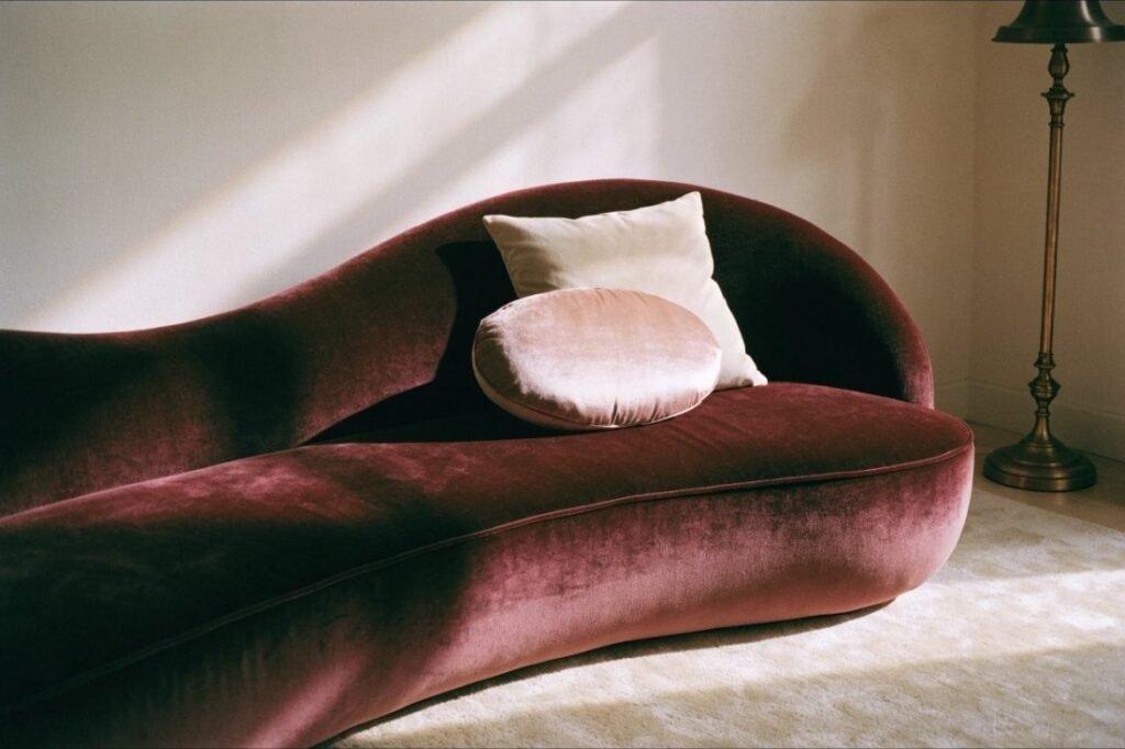 A deep burgundy velvet sofa with a curved sculptural back, styled with cream and blush cushions