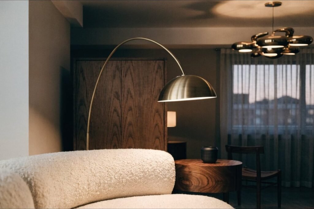 An antique brass arc floor lamp curving over a cream boucle sofa at dusk