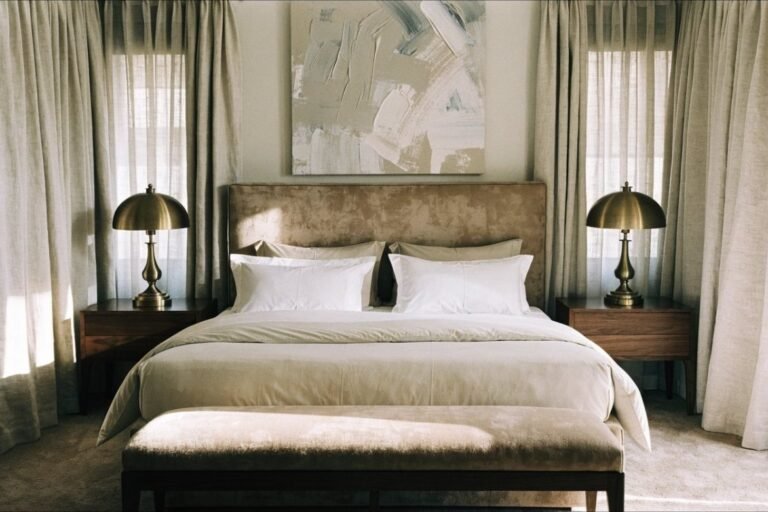A hotel-suite style bedroom with a tall upholstered headboard, symmetrical nightstands and brass lamps