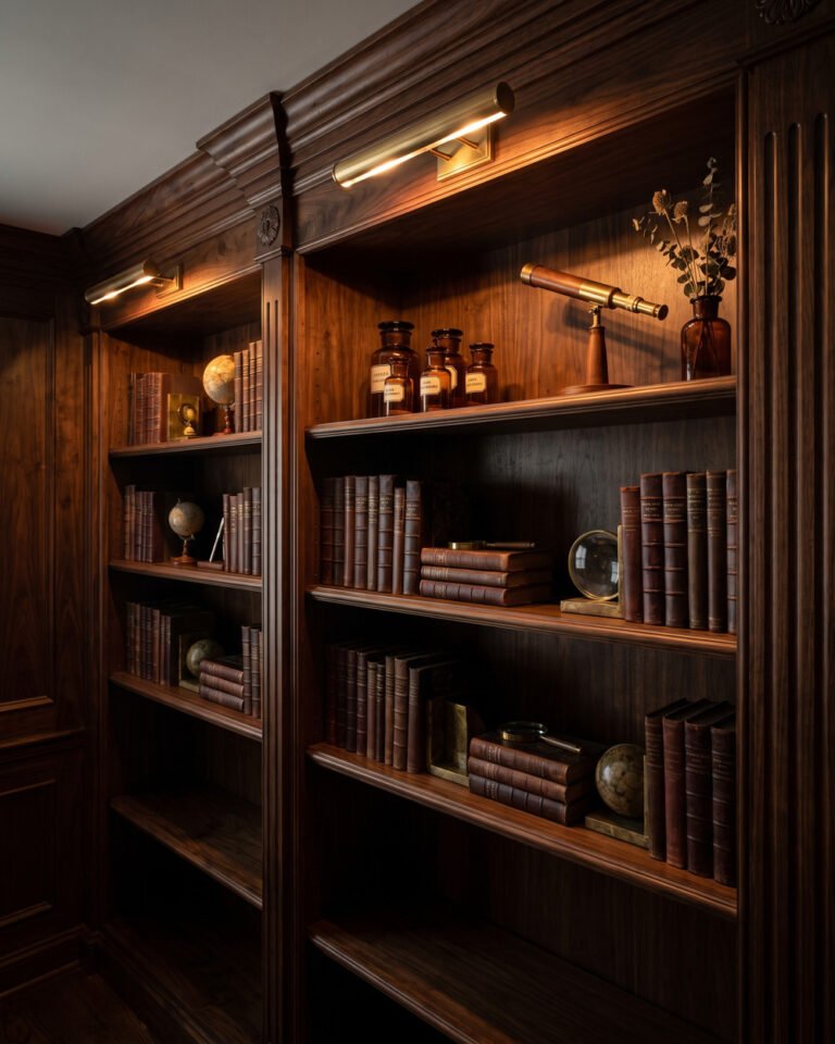 Dark wood bookshelf styled like a wizarding library with leather-bound volumes, brass candlesticks, amber apothecary bottles, a brass telescope and a small rechargeable picture light warming the top shelf.